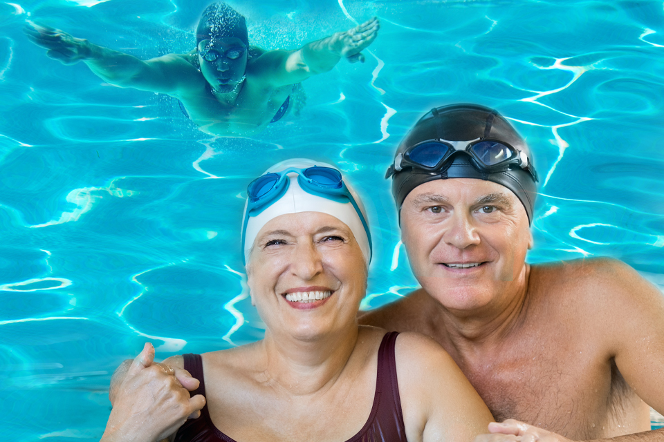 Imagem de duas pessoas equipadas com tocas e fatos de banho numa piscina com nadador em fundo da imagem