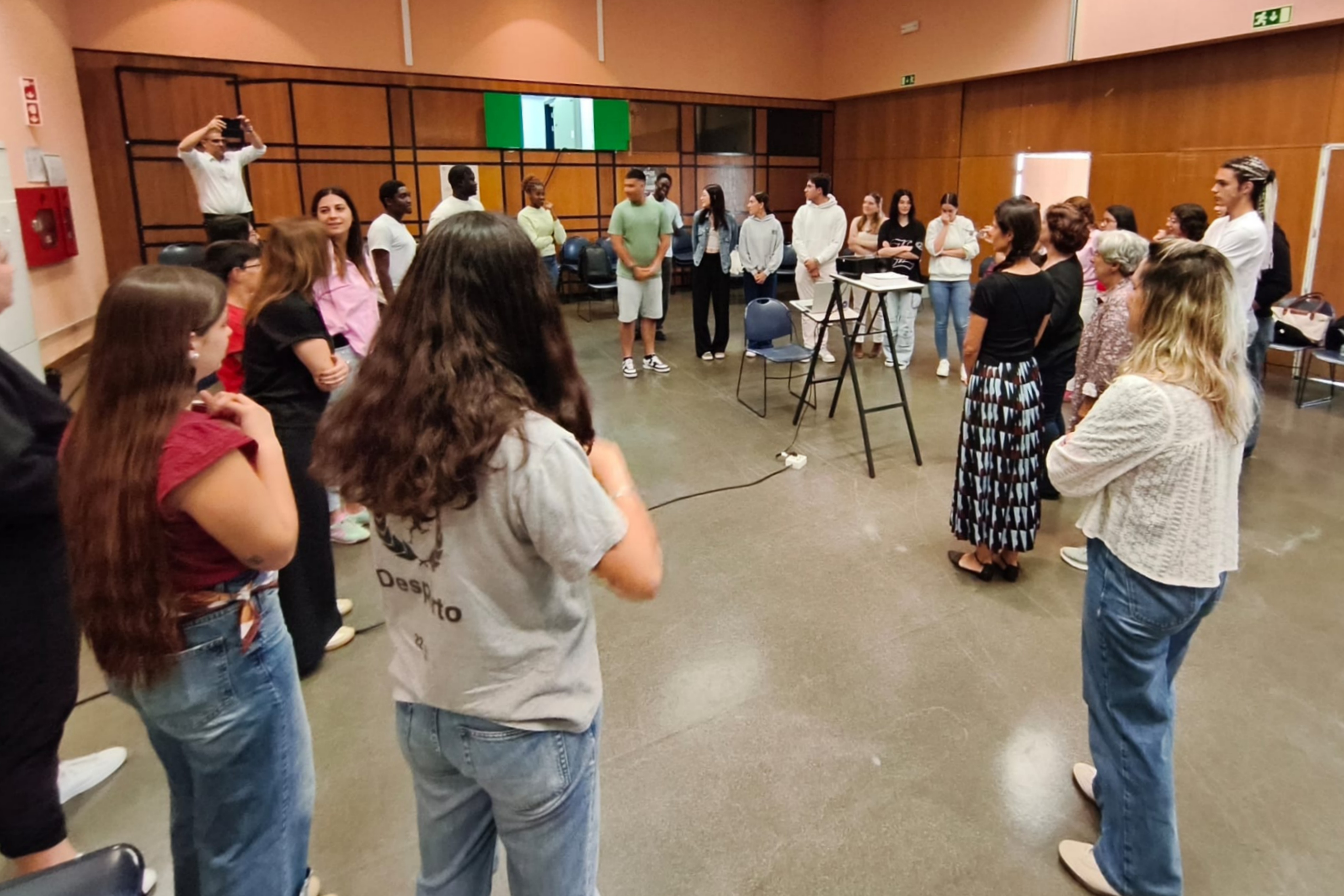 Jovens em pé posicionados em circulo a realizar uma dinâmica de quebra-gelo.