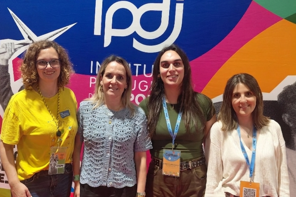 Quatro pessoas na fotografia, com o banner do IPDJ no plano de fundo