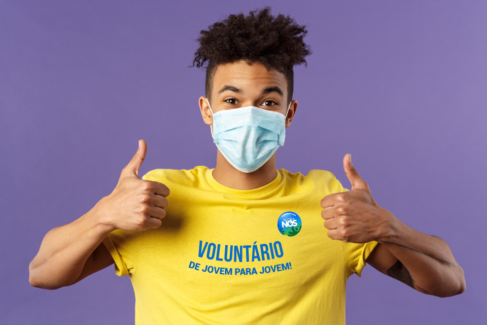Jovem com máscara e t-shirt amarela onde se lê "voluntário de jovem para jovem"