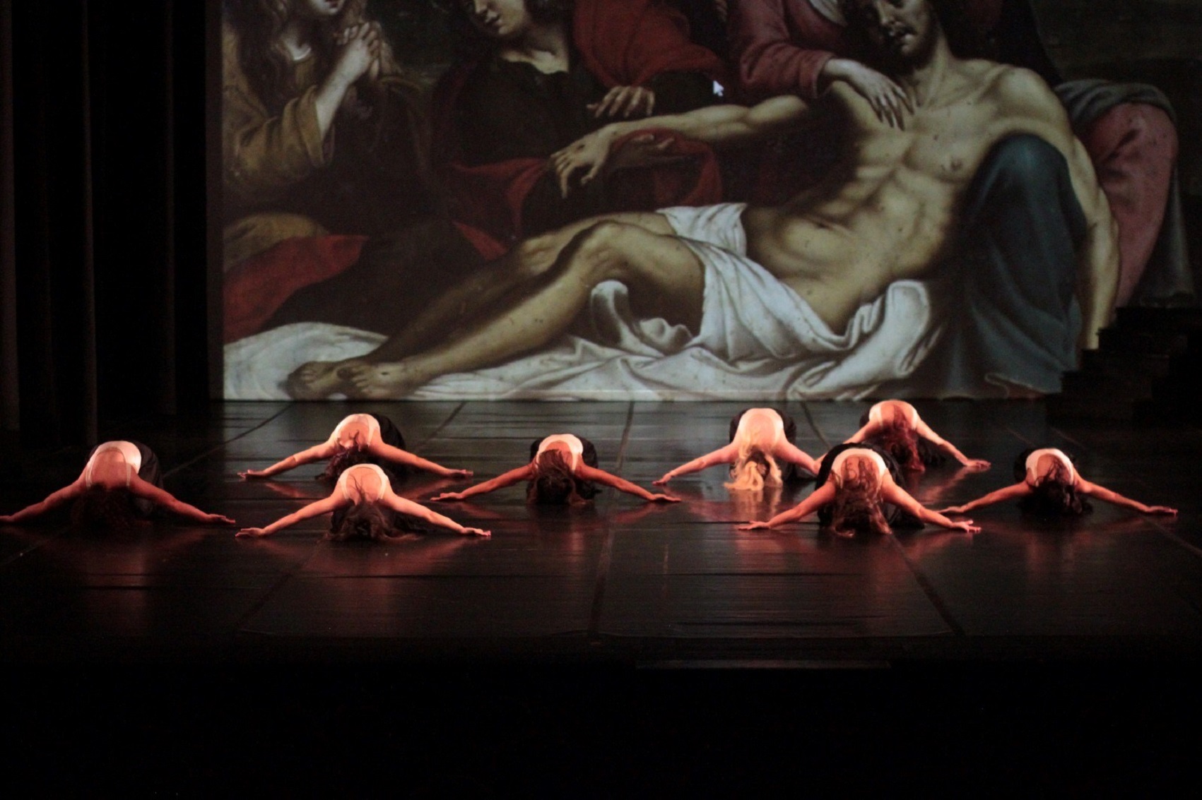 Oito bailarinas em palco, tendo como cenário uma imagem de uma pintura barroca. 