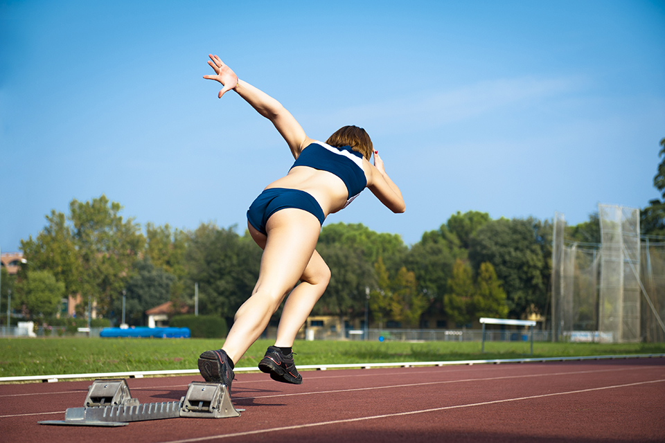 mulher de costas a iniciar corrida numa pista de atletismo