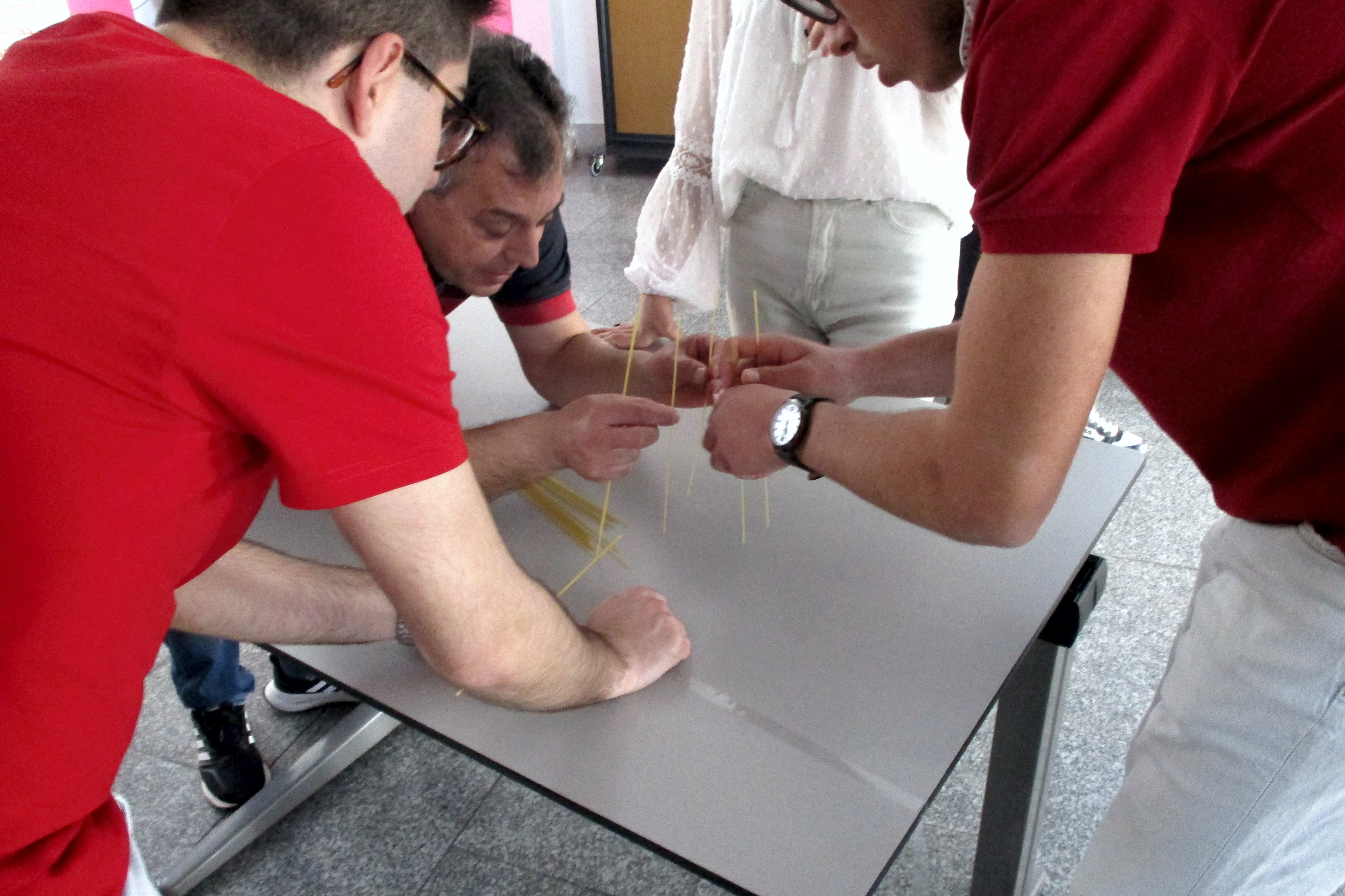 Grupo de jovens e um professor a participarem no Workshop sobre associativismo, a tentarem construir, em cima de uma mesa, uma torre de esparguete. Atividade realizada no IPDJ de Évora. 