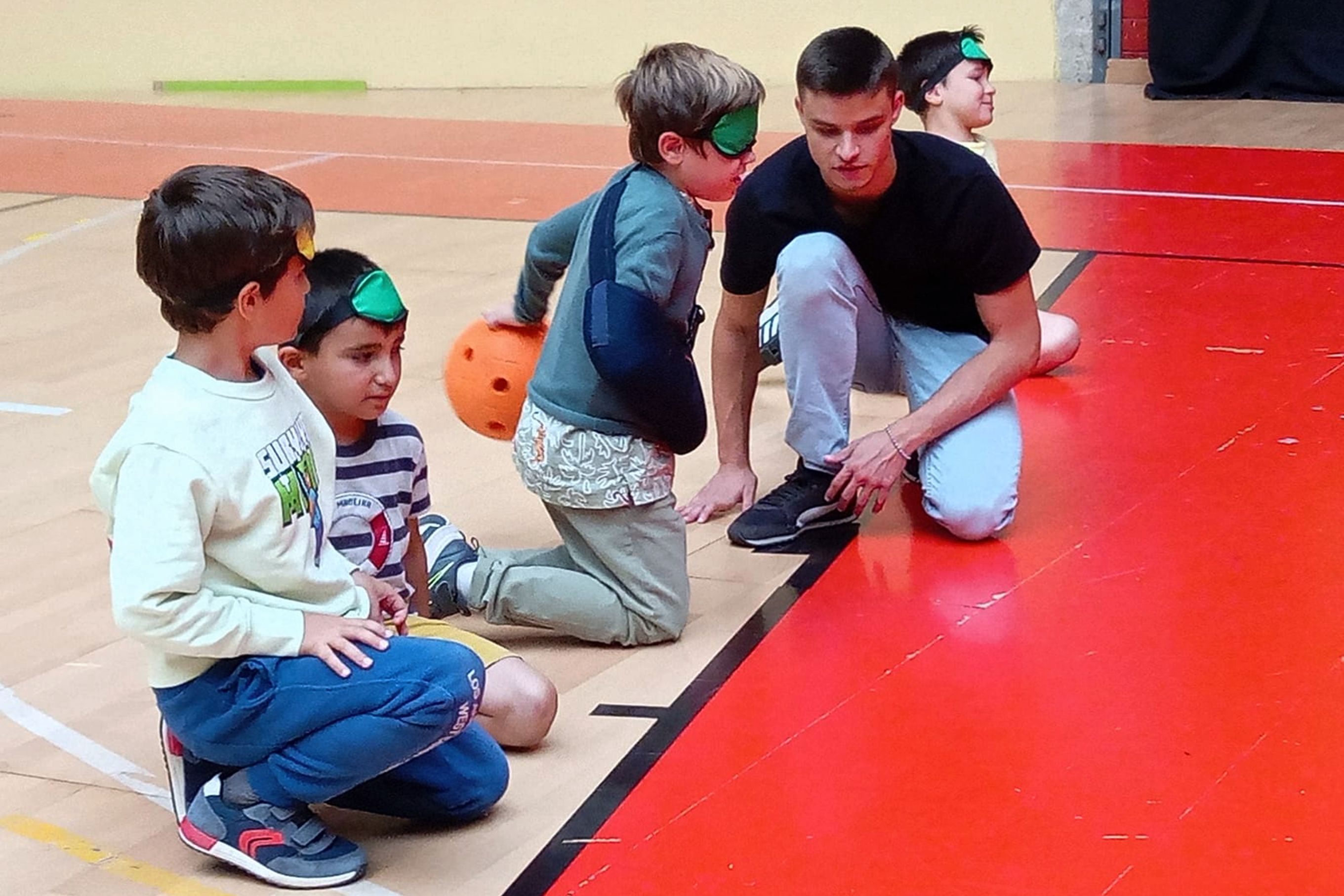 Três crianças e um jovem voluntário, na Arena D' Évora, a participarem na atividade de Goalball.