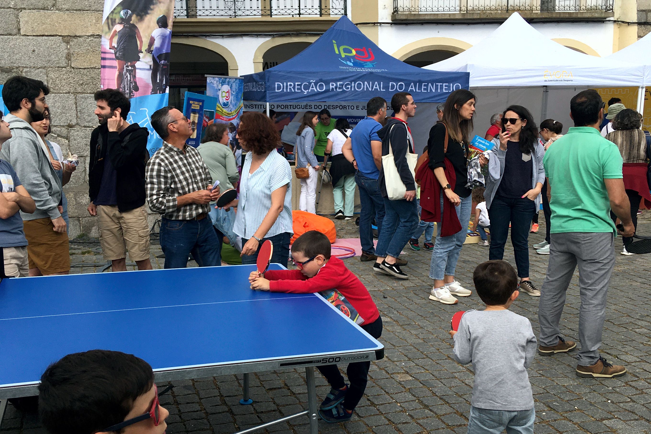 Várias pessoas na Praça do Giraldo a assistirem às atividades, e crianças a jogarem ténis de mesa.