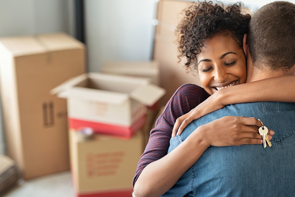 Jovem casal abraçado. A rapariga tem duas chaves na mão.