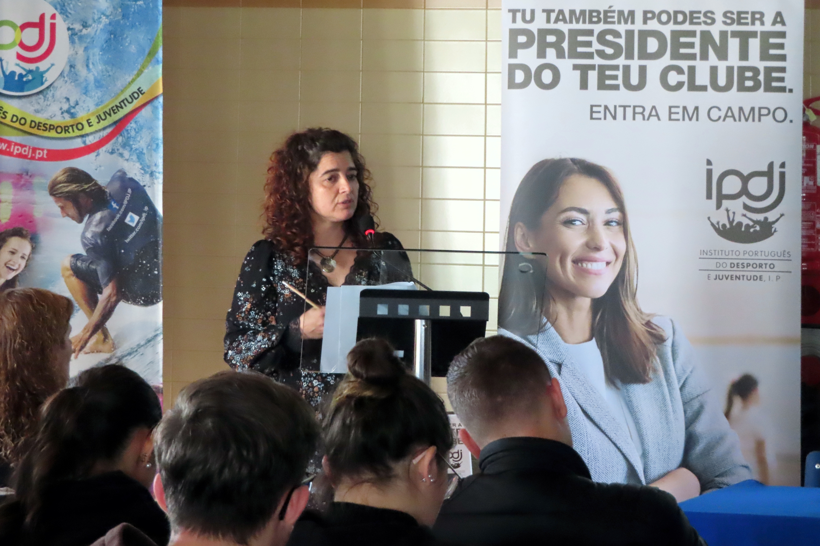 Técnica do IPDJ Rita Felícia a apresentar a campanha, tendo como fundo um Roll-Up do IPDJ e outro da Campanha «Tu também podes ser presidente do teu clube».