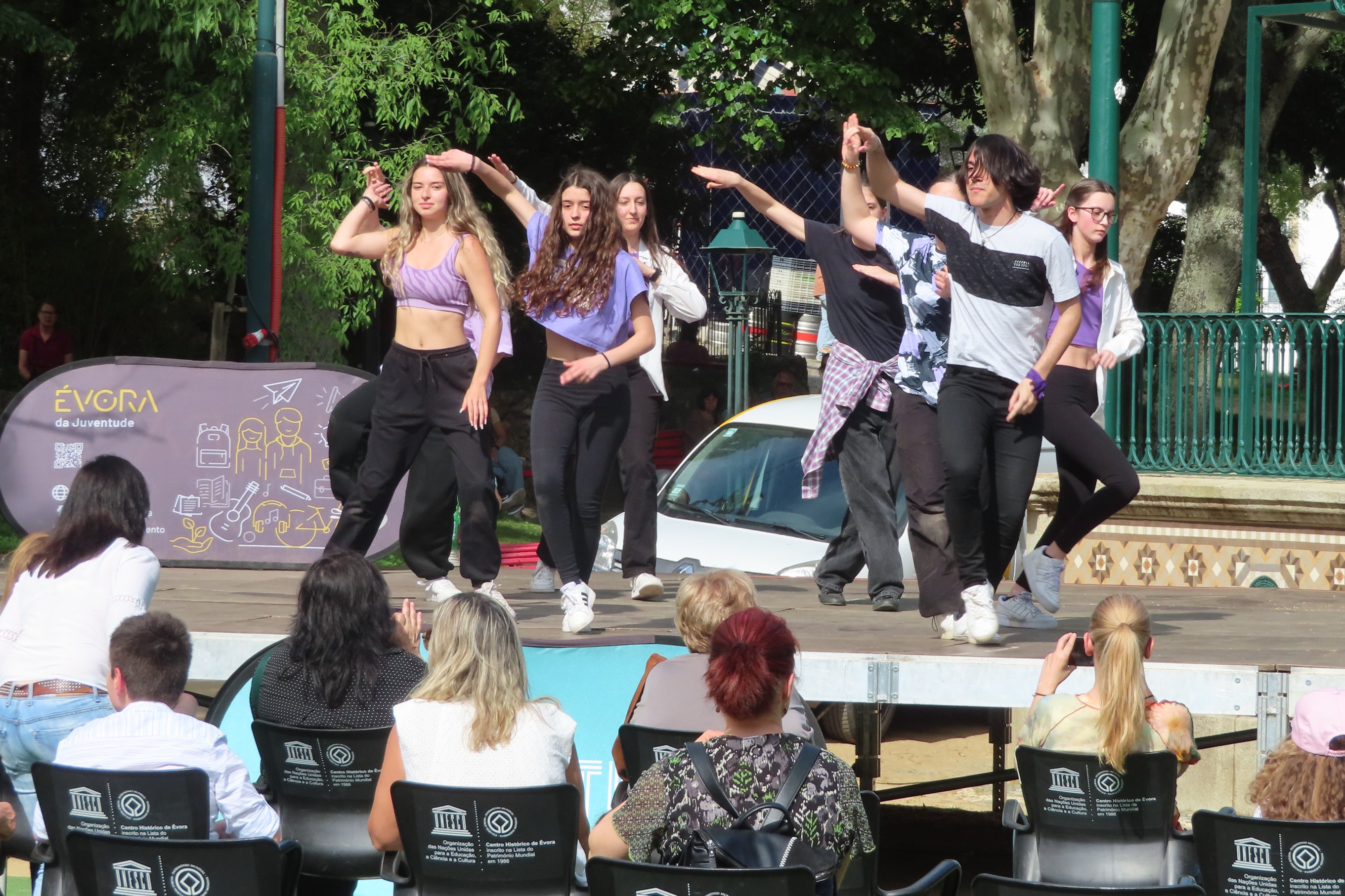 Jovens em palco, no Jardim Público de Évora a realizarem uma coreografia de dança com algum público a assistir.