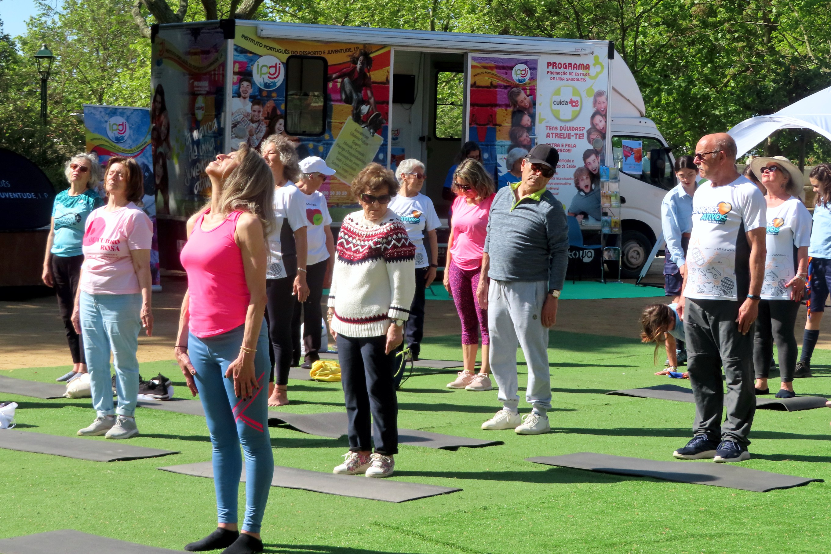 Grupo de pessoas no Jardim Público de Évora, a participarem numa atividade física, junto à Unidade Móvel Cuida-te+.