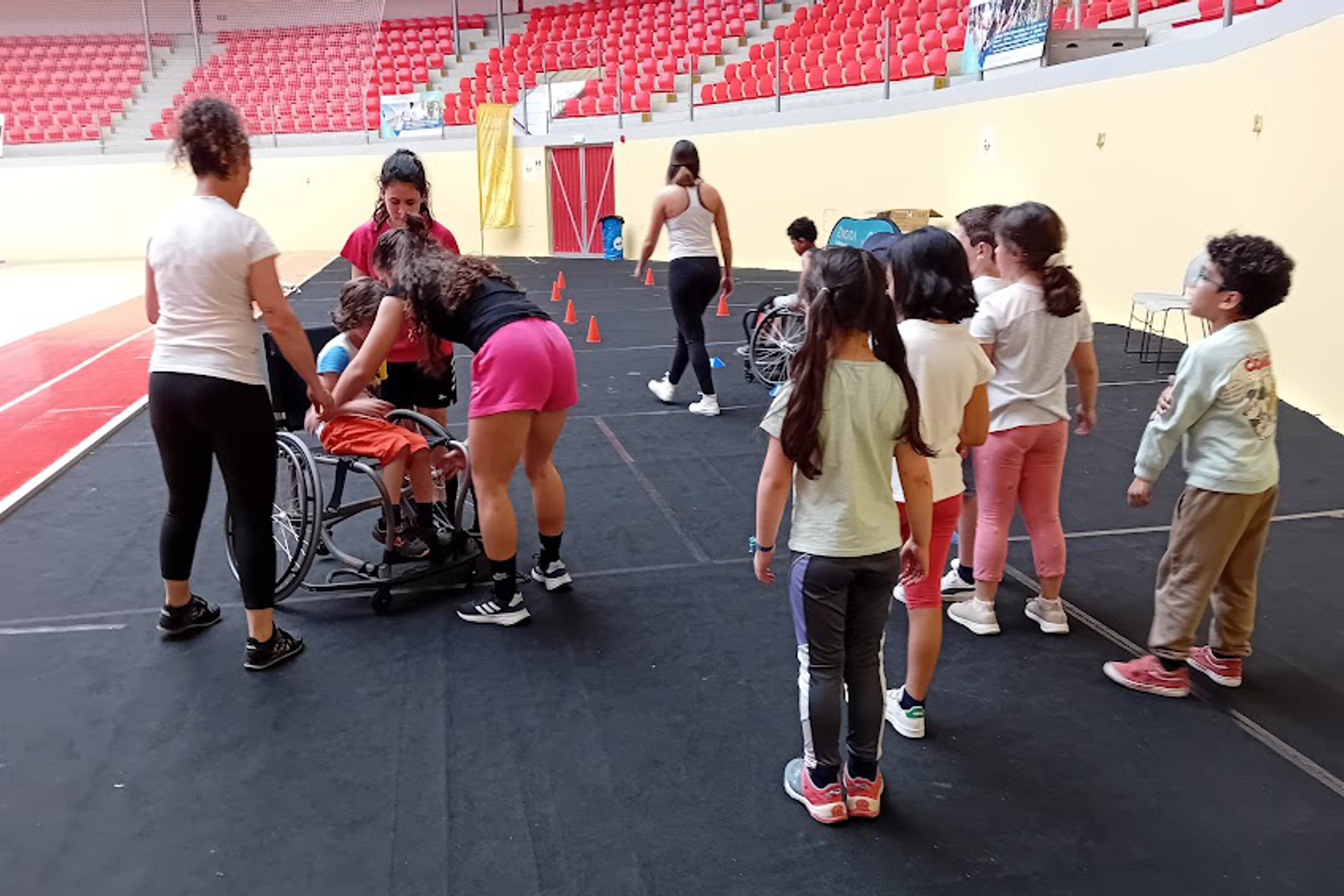 Grupo de crianças na Arena D'Évora a experimentarem como é andar em cadeira de rodas, orientadas/apoiadas pelos alunos da Universidade de Évora.
