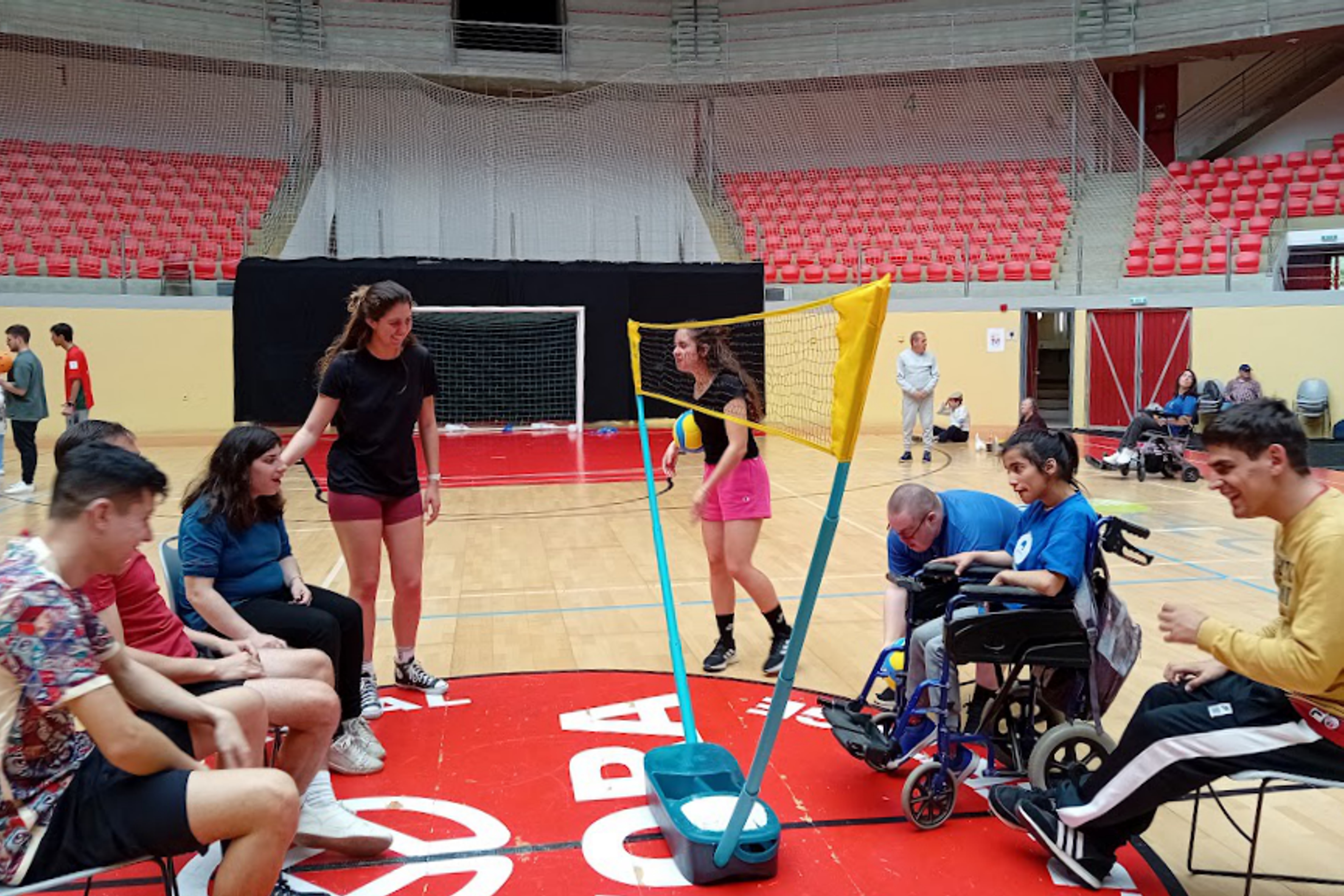 Grupo de jovens na Arena D'Évora, com mobilidade reduzida a jogarem vóleibol, com um grupo de jovens sem problemas de mobilidade.