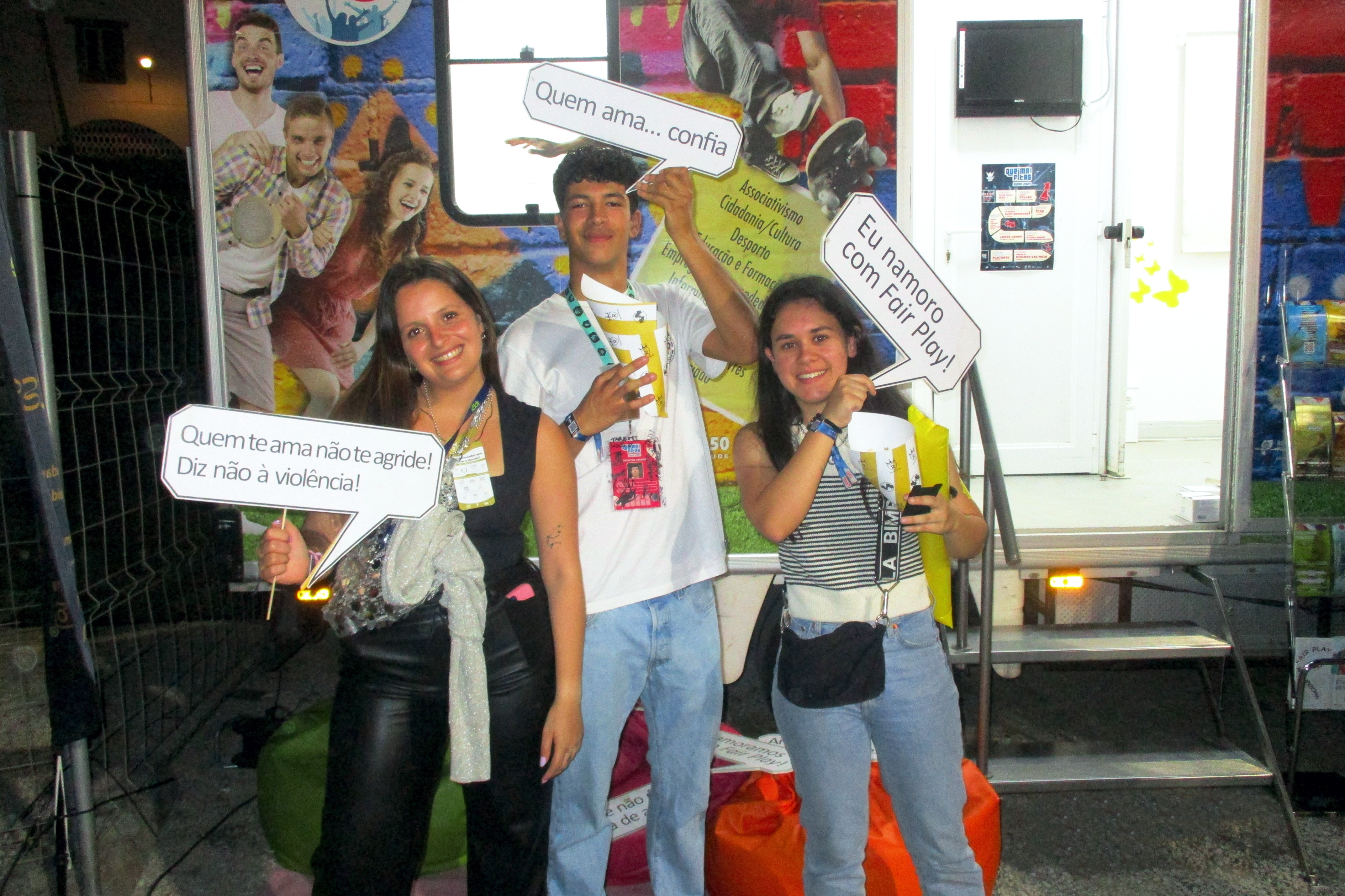 Duas jovens e um jovem, junto à Unidade Móvel Cuida-te+, com um «balão» cada um, sobre o projeto «Namorar com Fair Play».
