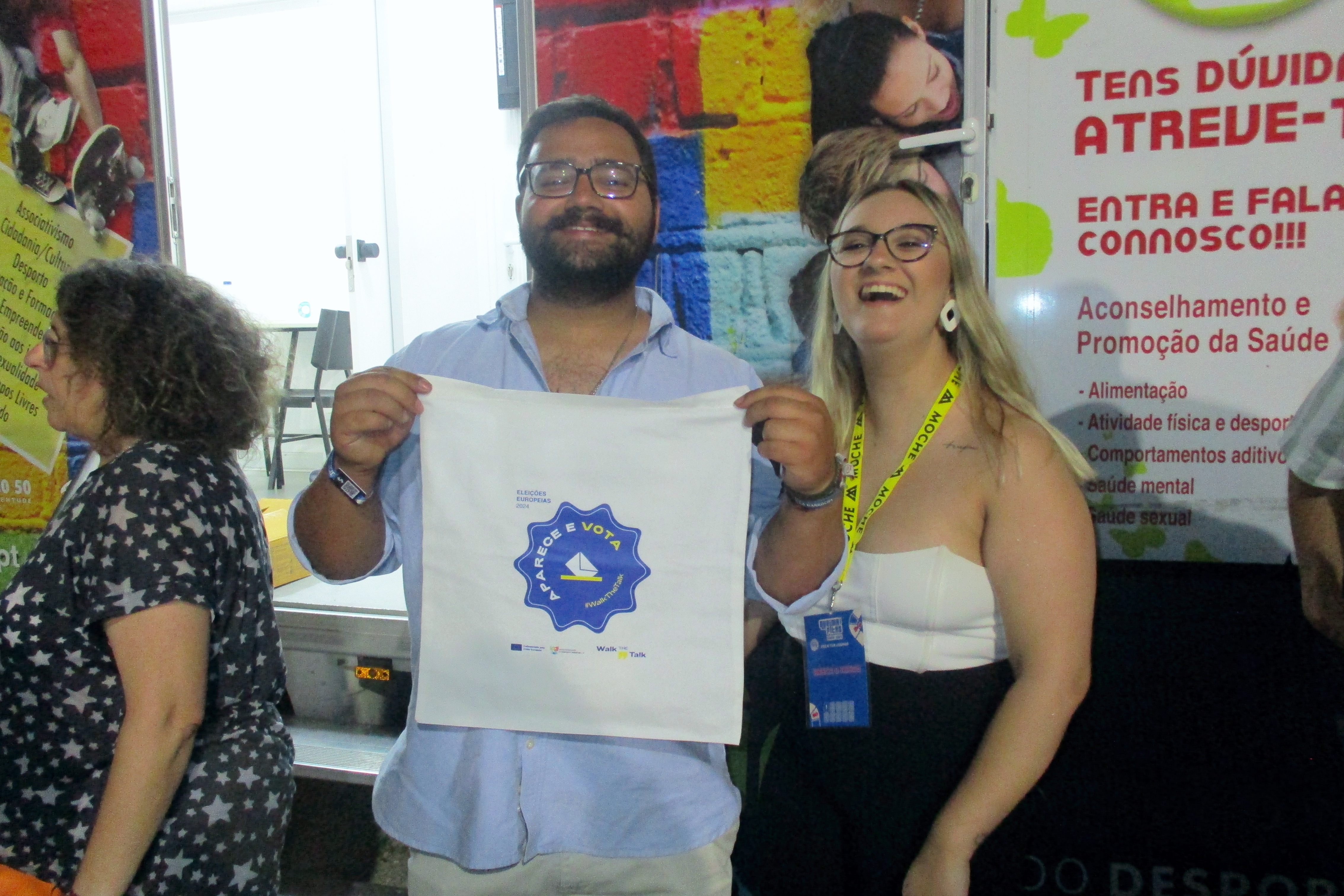 Jovem junto à Unidade Móvel Cuida-te+, a mostrar o saco, da Campanha Walk The Talk», na companhia das voluntárias Inês Costa e Rosário Ramalho.