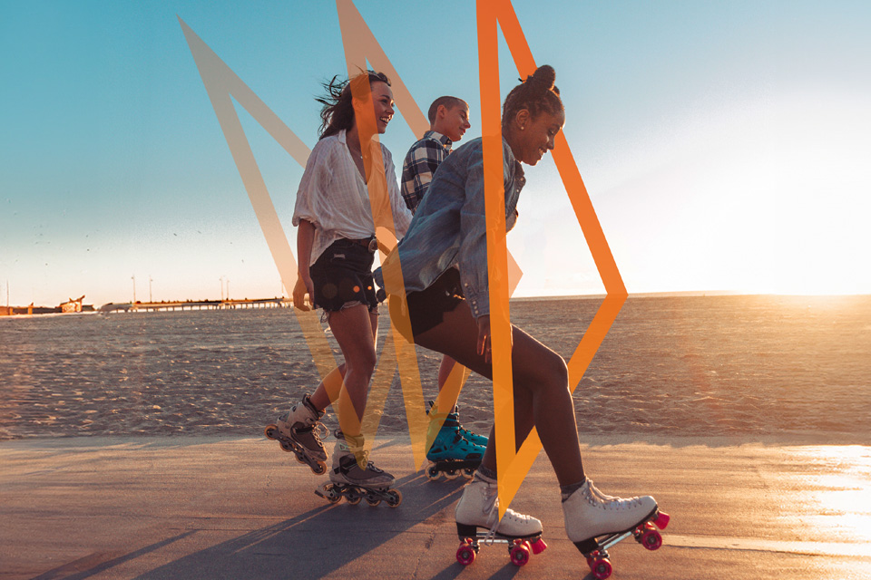 Três jovens a andar de patins numa estrada ao lado duma praia.