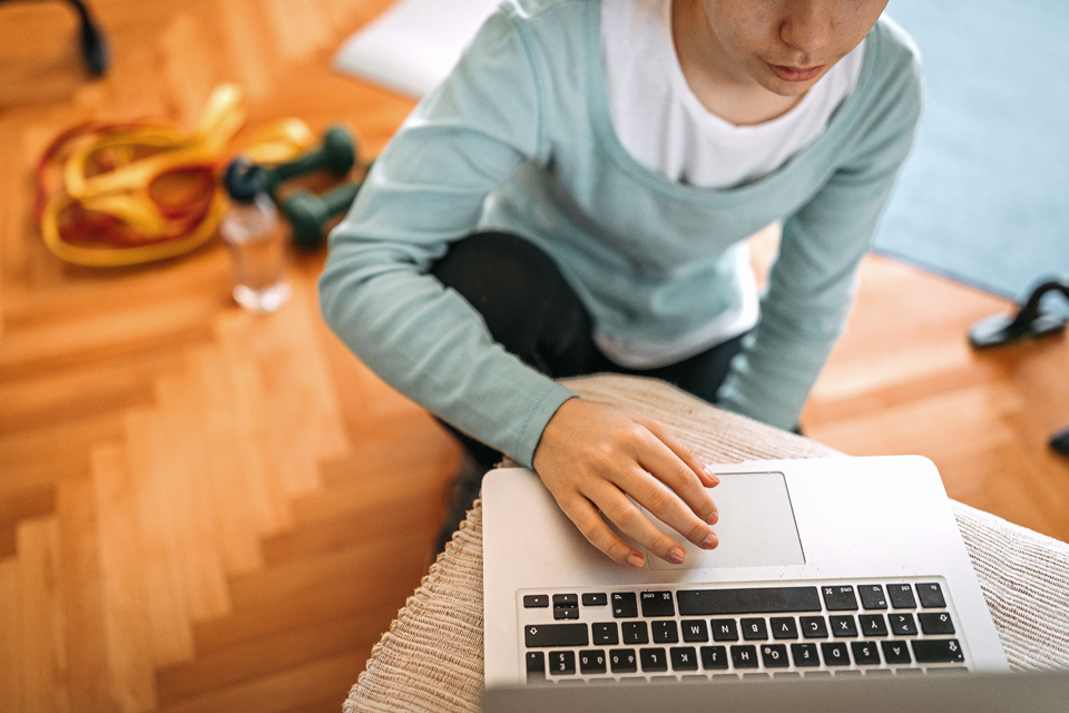 imagem de jovem em frente a um portatil e no chão espalhados vários utensilios usados em atividades fisicas