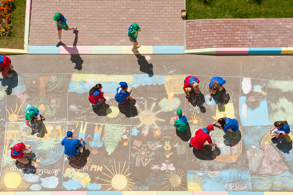 vista aérea de jovens a pintar com giz no chão de um espaço externo.