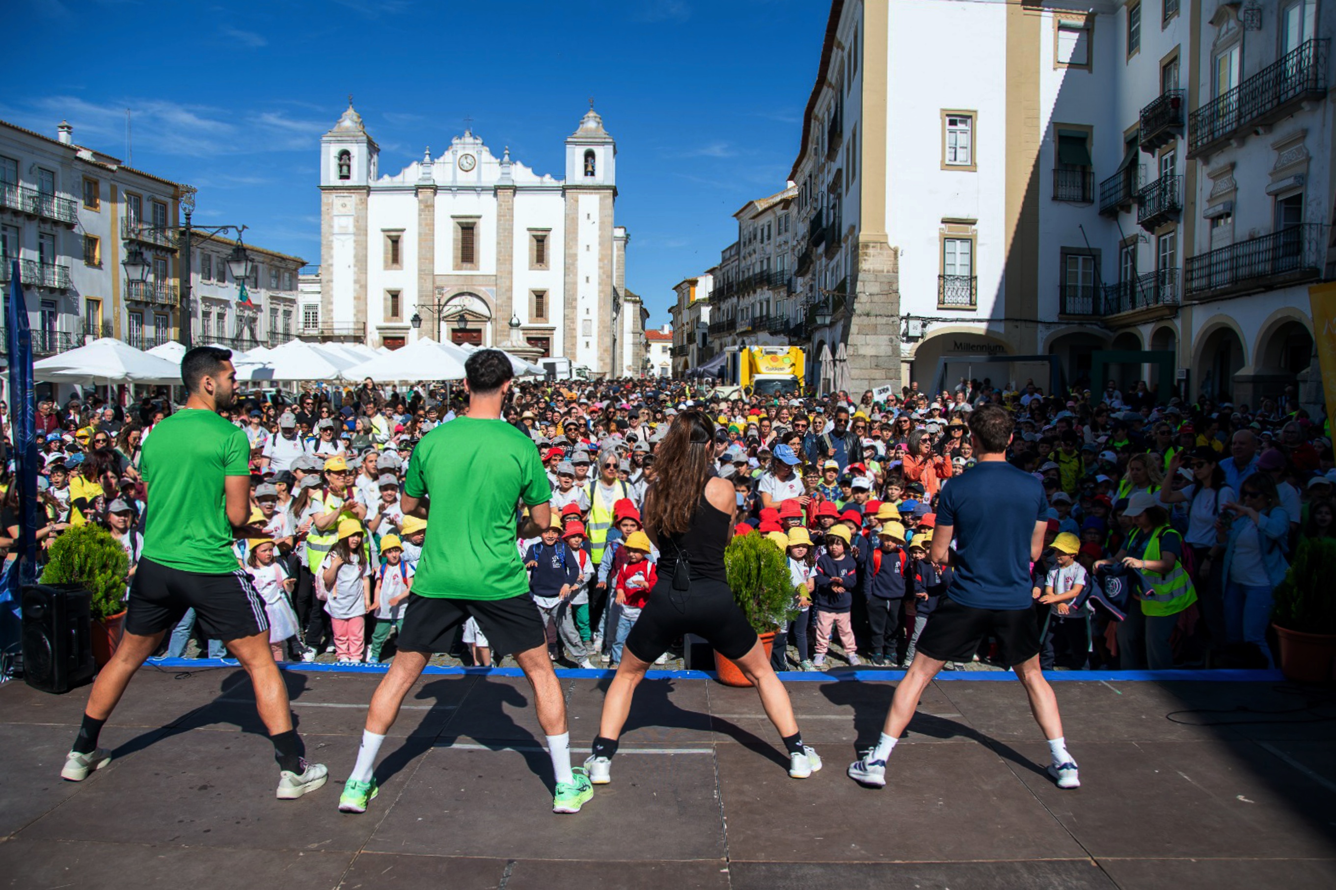 Participantes e público na sessão de aquecimento na Praça do Giraldo antes da Caminhada das Escolas, dinamizada por técnicos de desporto.