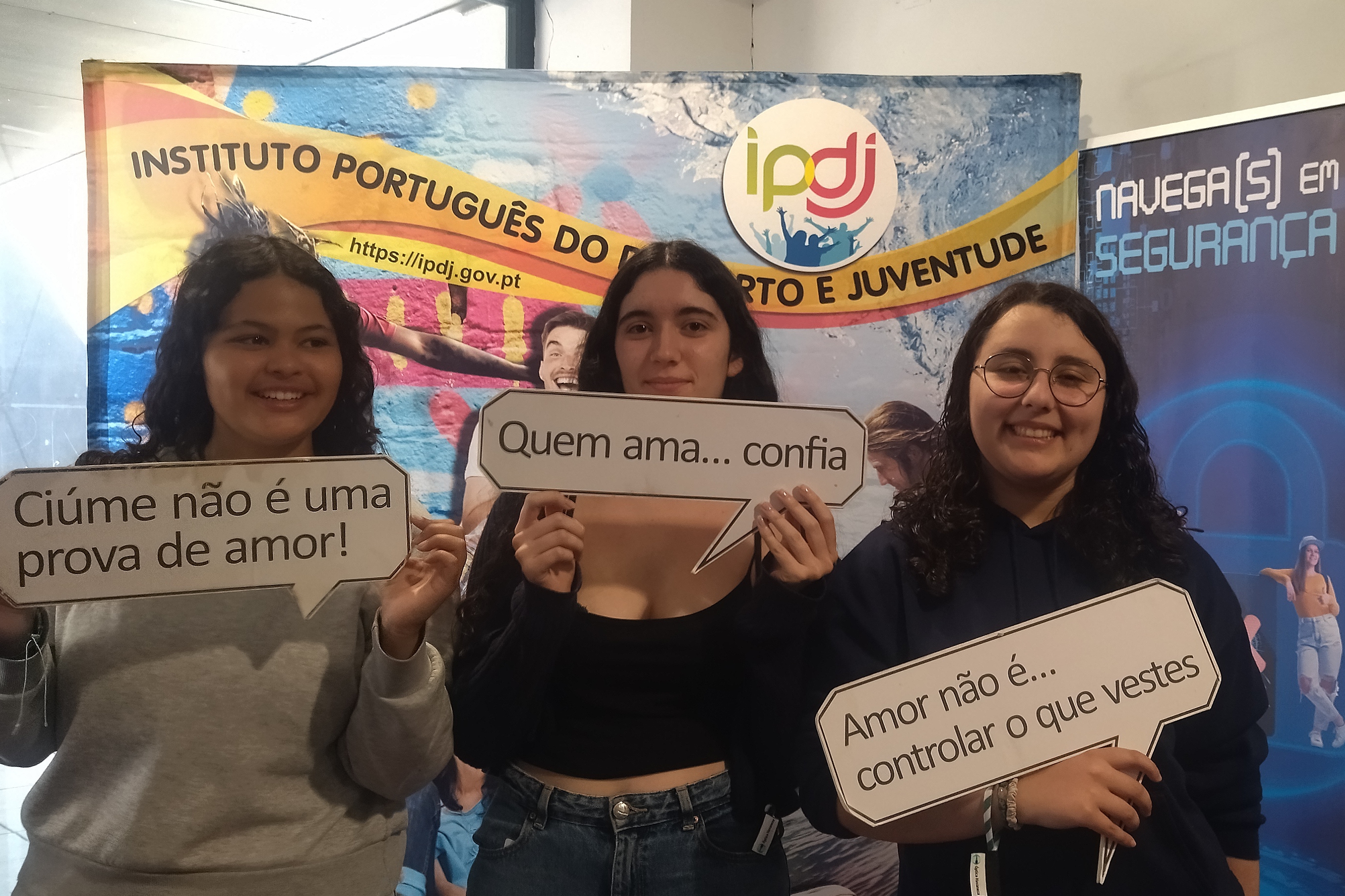 Três jovens no Stand IPDJ a participarem nas atividades IPDJ, em particular no projeto «Namorar com Fair Play», segurando alguns slogans deste projeto.