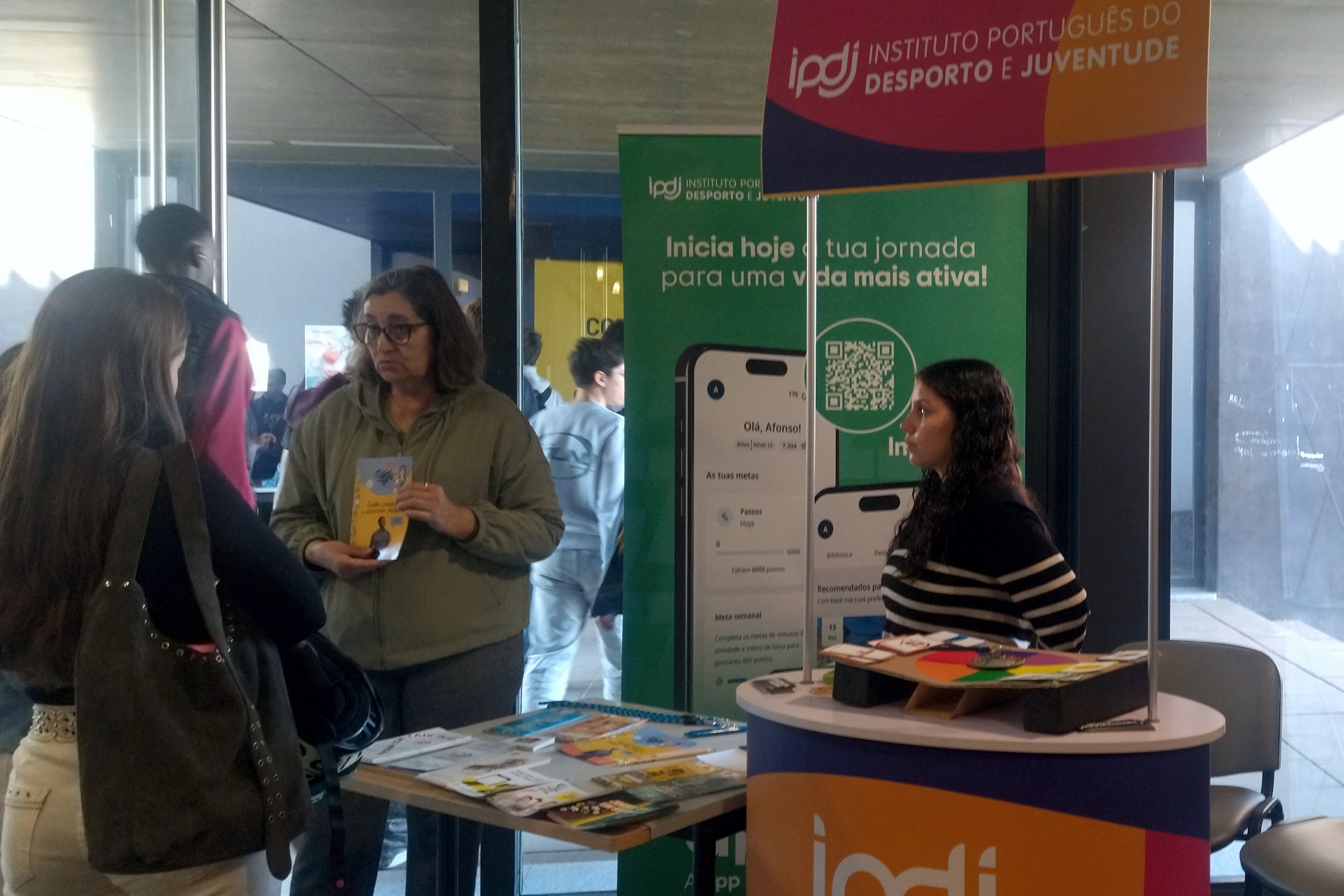 Jovens junto ao stand do IPDJ a participarem nas atividades dinamizadas pela técnica do IPDJ de Évora, Anabela Santos e por uma voluntária IPDJ, aluna da Escola Secundária Severim de Faria.