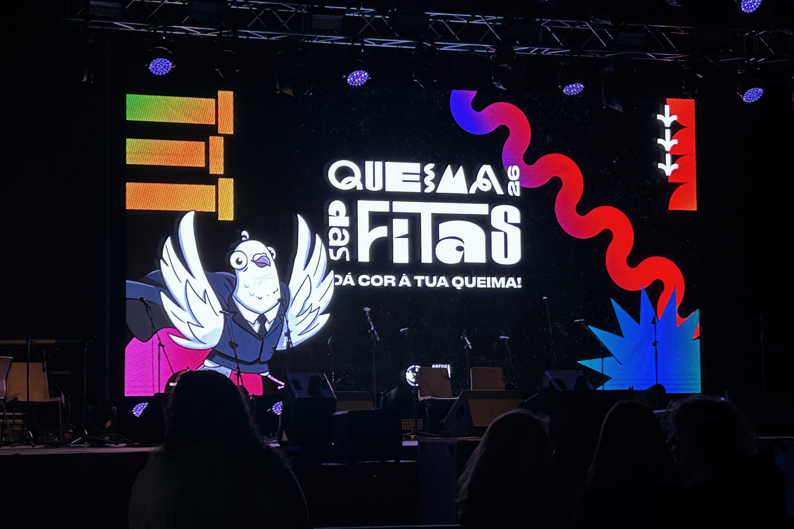 Cartaz alusivo à «Queima das Fitas», em fundo preto com algum lettering, e hologramas em branco, vermelho, azul e laranja.