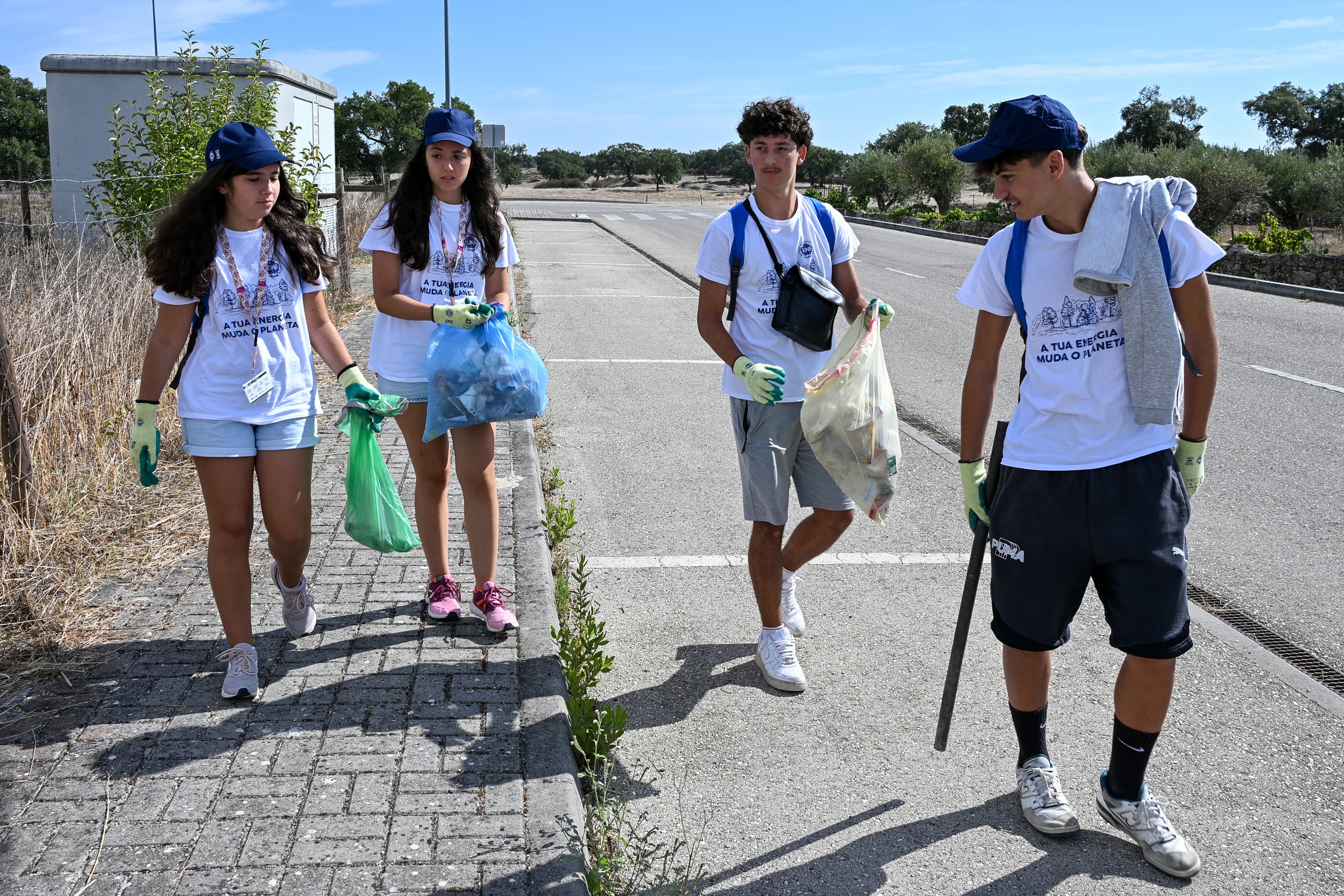 Quatro jovens voluntários a recolherem o lixo espalhado junto à estrada.