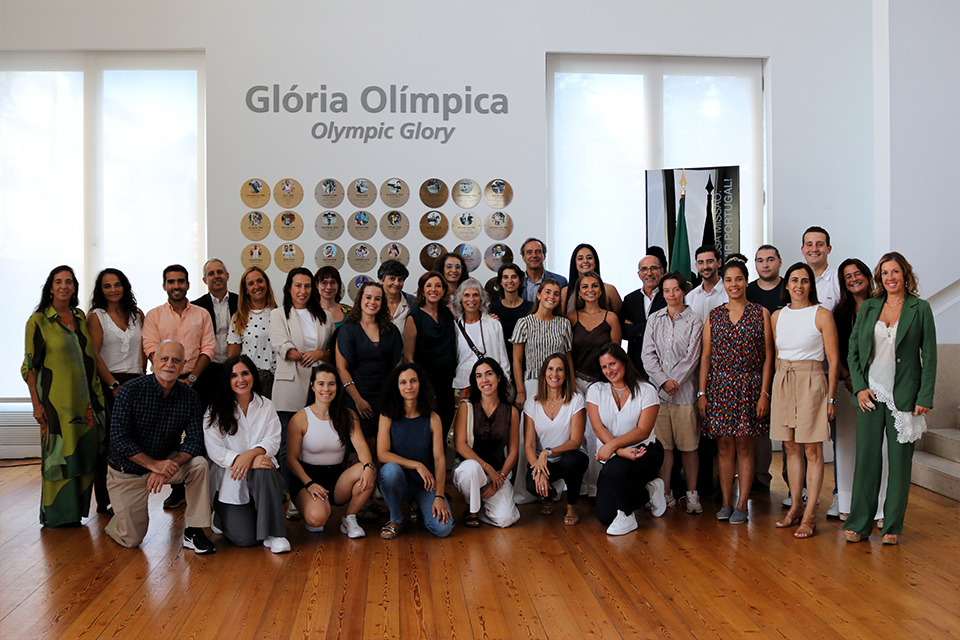 Fotografia de grupo dos participantes da 4.ª edição do Programa Novas Lideranças  Para um Desporto mais Igual, no espaço Glória Olímpica do Comité Olímpico de Portugal. Ao fundo são visíveis o painel comemorativo e as bandeiras de Portugal e do COP.