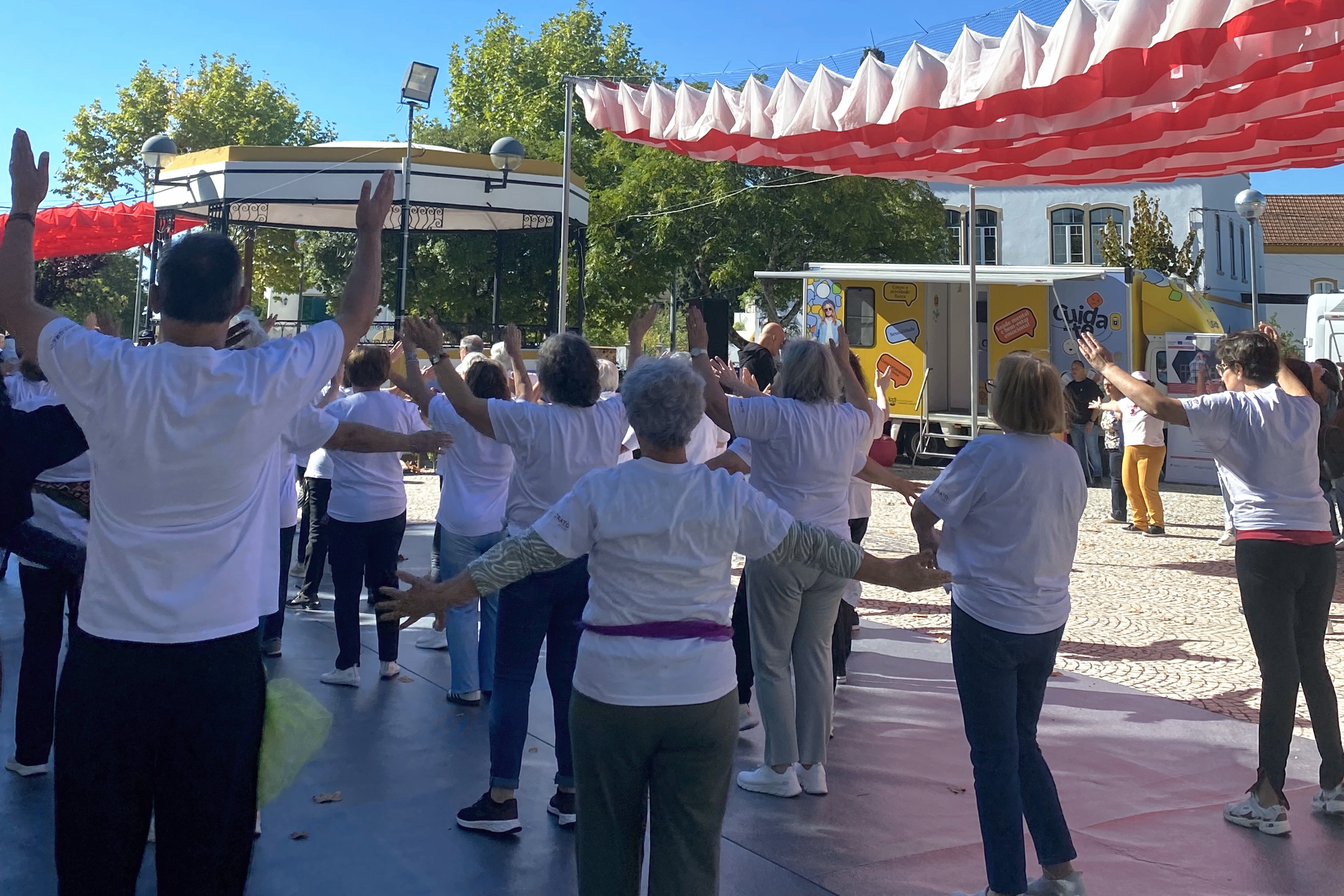 Grupo de pessoas a participarem numa atividade física dinamizada pela organização, tendo ao fundo a Unidade Móvel do Programa Cuida-te.